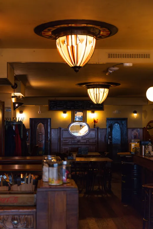 Art-deco plafondlamp en bollampen boven het donkere houten interieur van het café.