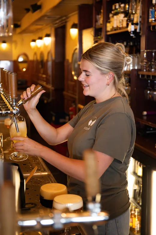 Medewerker tapt een vers glas bier achter de bar van Café de Roemer.