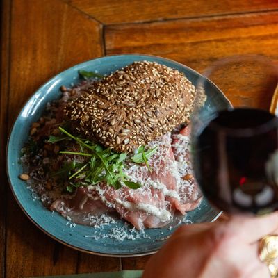 Een bord carpaccio met pijnboompitten en rucola op een blauw bord.