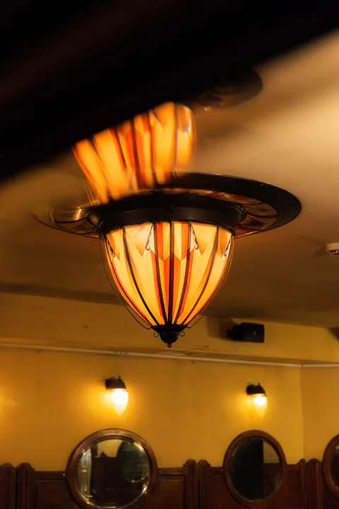 Waaiervormige art-decoplafondlamp die amberkleurig licht geeft, met daaronder wandlampen en spiegels.