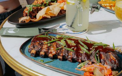 Een tafel met spareribs, een gedeelde plank, friet en drinken, met gasten eromheen.