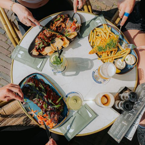 Bovenaanzicht van een tafel waar borden met friet en gerechten worden gedeeld.