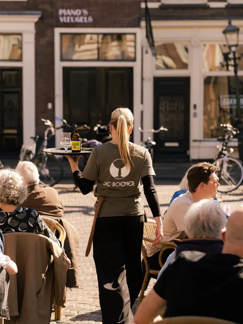 Een medewerker brengt drankjes naar de gasten op het terras.