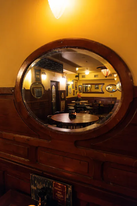 Bolle ronde spiegel in donkere houten lambrisering, met het café weerspiegeld in de bolling.