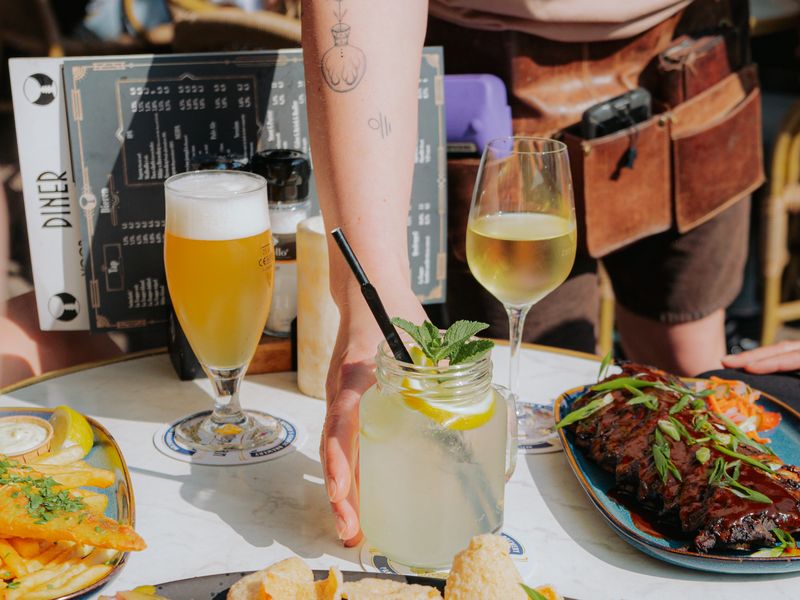 Bier, verse limonade en een lunchgerecht op een marmeren terrastafel in de zon.